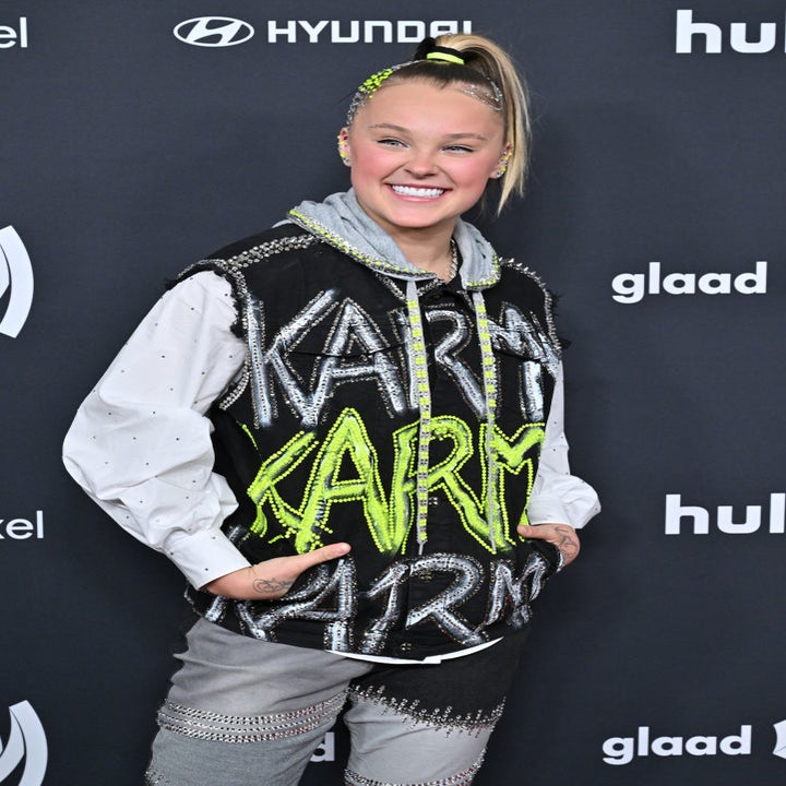 JoJo Siwa smiling on the GLAAD red carpet, wearing a sporty, embellished outfit with the word "KARMA" in large letters
