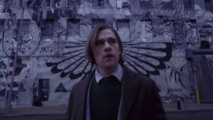Quentin Coldwater stands in front of a graffiti’d wall in a scene from The Magicians.