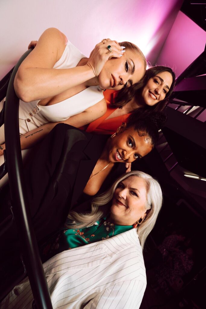 Four women gather in close at a skewed angle for a portrait.