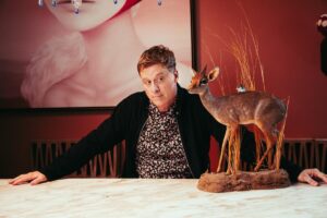 Alan Tudyk gives side-eye to a small deer statue in a portrait.