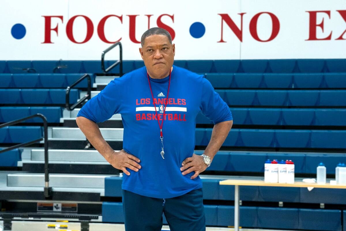 A coach with his hands on hips looking at the basketball court.