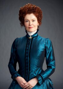 Rebecca Wisocky as Hetty, wears a high-necked, long-sleeved dress