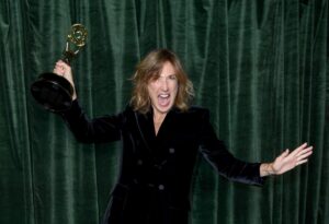 Jessica Hobbs holds an Emmy statuette up high in one hand and smiles widely.