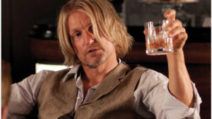 Woody Harrelson as Haymitch toasts with a drink