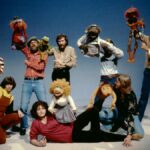 Jim Henson and his team hold up a variety of his Muppet creations