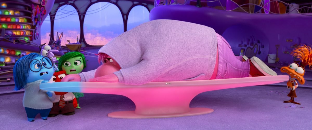 A big emotion in a hooded sweatshirt lies across the console in Inside Out 2