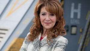 Bonnie Langford stands in front of a futuristic looking building in a press release photo tied to her return to Doctor Who.