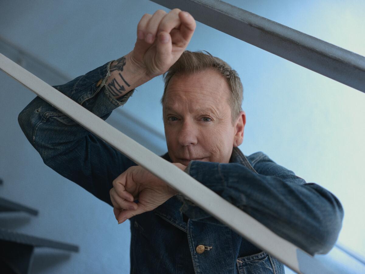 Kiefer Sutherland leans on stair railings for a portrait.