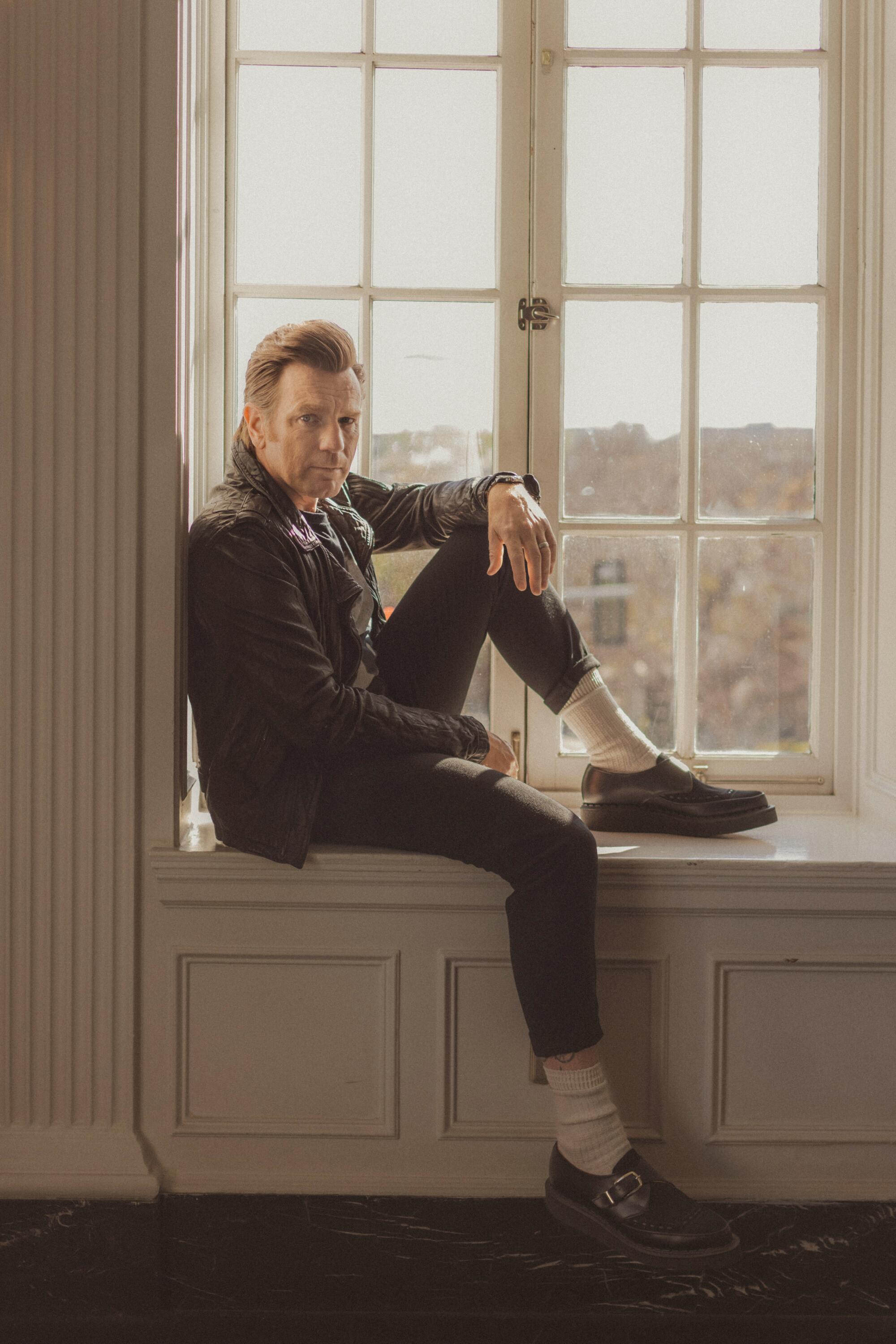 Ewan McGregor sits in a windowsill with one knee raised for a portrait.