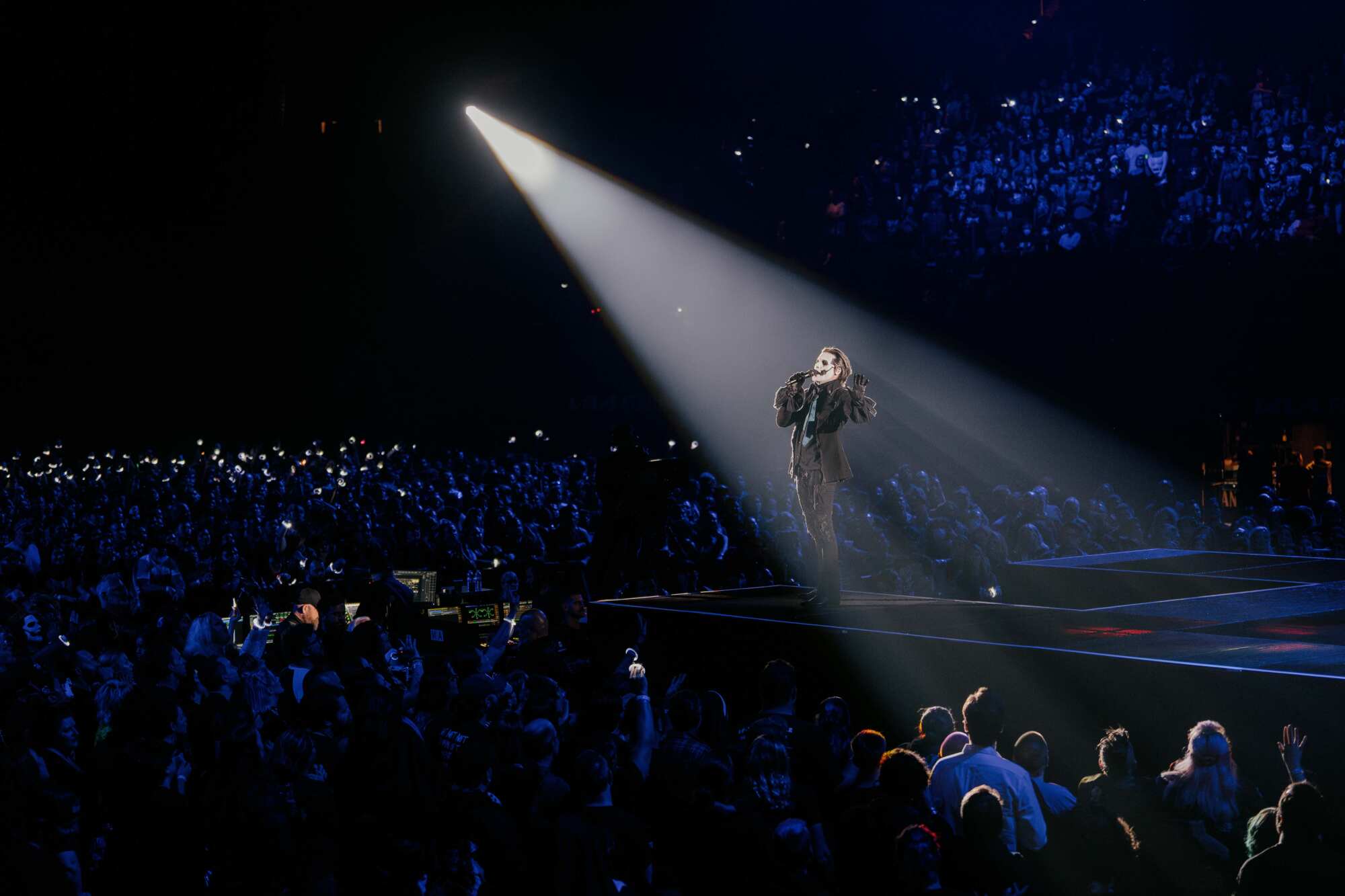 A singer in a spotlight performs in front of a huge crowd.