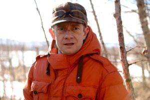 A man in a cap and heavy coat stands outside looking startled in "Fargo," Season 1.