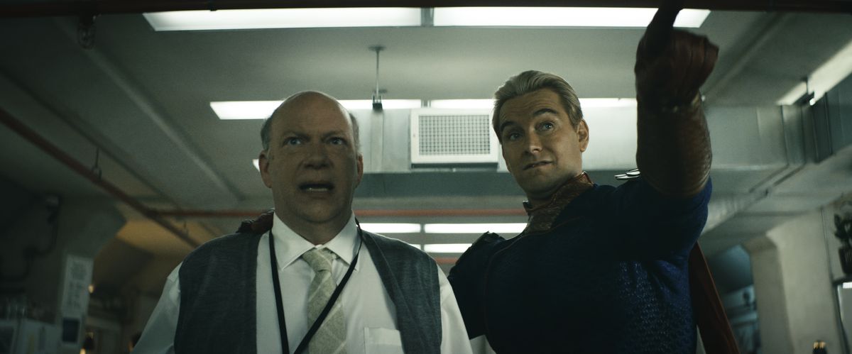 Homelander, his arm around a terrified scientist, points at something off-screen in a scene from The Boys season 4.