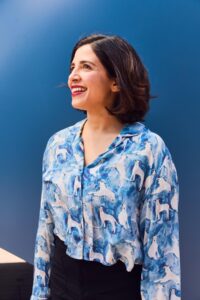Natasha Kline standing in front of a blue wall wearing a blue and white blouse