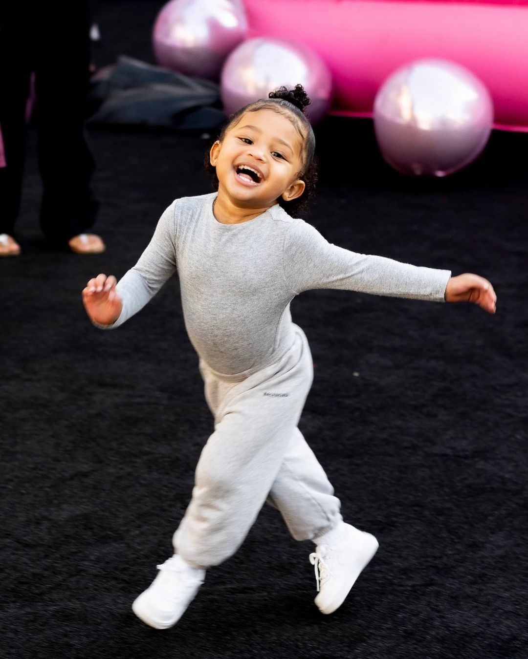 Stormi Webster flashes a smile while rocking a "groutfit," a monochromatic outfit made up of different shades of grey clothings, along with fresh white sneakers