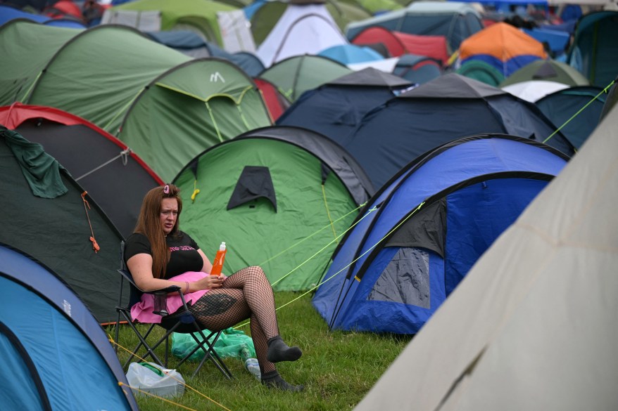 A festival-goer sitting by tents during the third day of the Glastonbury Festival at Worthy Farm, Somerset, England