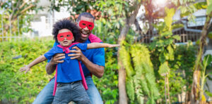 Father's Day - Happy black African American father daughter playing home outdoor. Afro man carry piggyback little toddler super hero boy. Cheerful family bonding together fatherâs day concept banner with copy space
