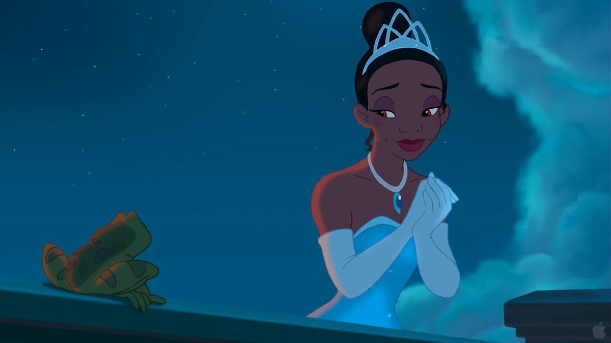 Tiana, a Black woman in a tiara, silver gown, and white opera gloves, clasps her hands together and smiles at a frog next to her in Disney’s The Princess and the Frog