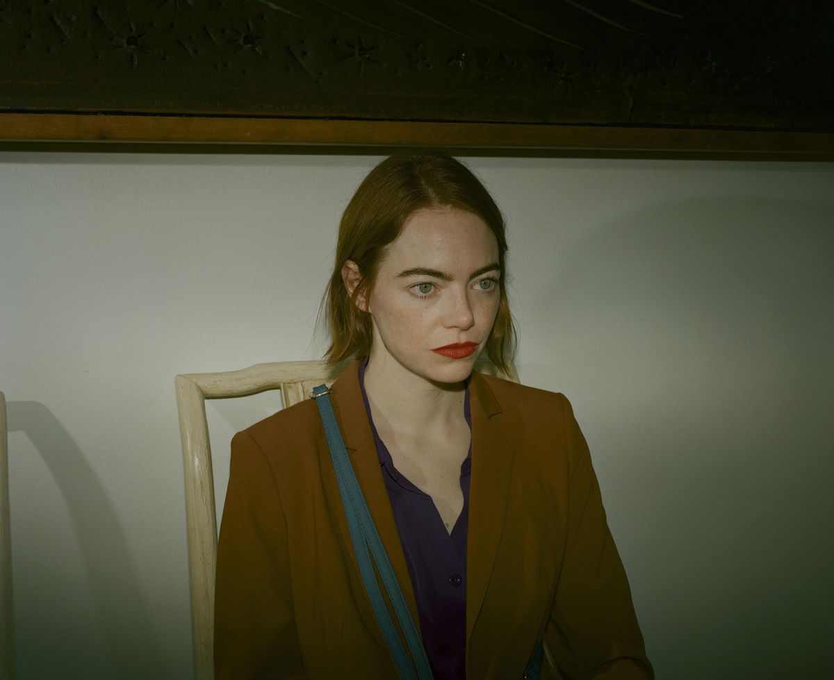 Emma Stone sits in a chair, lit starkly, looking troubled, with shortish red hair and scarlet lipstick, in Kinds of Kindness