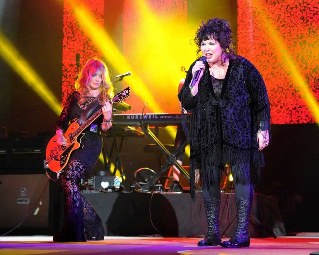 Ann Wilson singing into a microphone and Nancy Wilson playing guitar on stage during the Heartbreaker Tour's opening night, 2013.