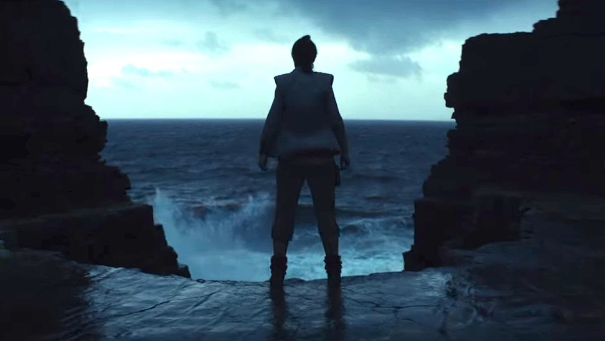 Rey stands in a cave entrance looking out at crashing waves in The Last Jedi