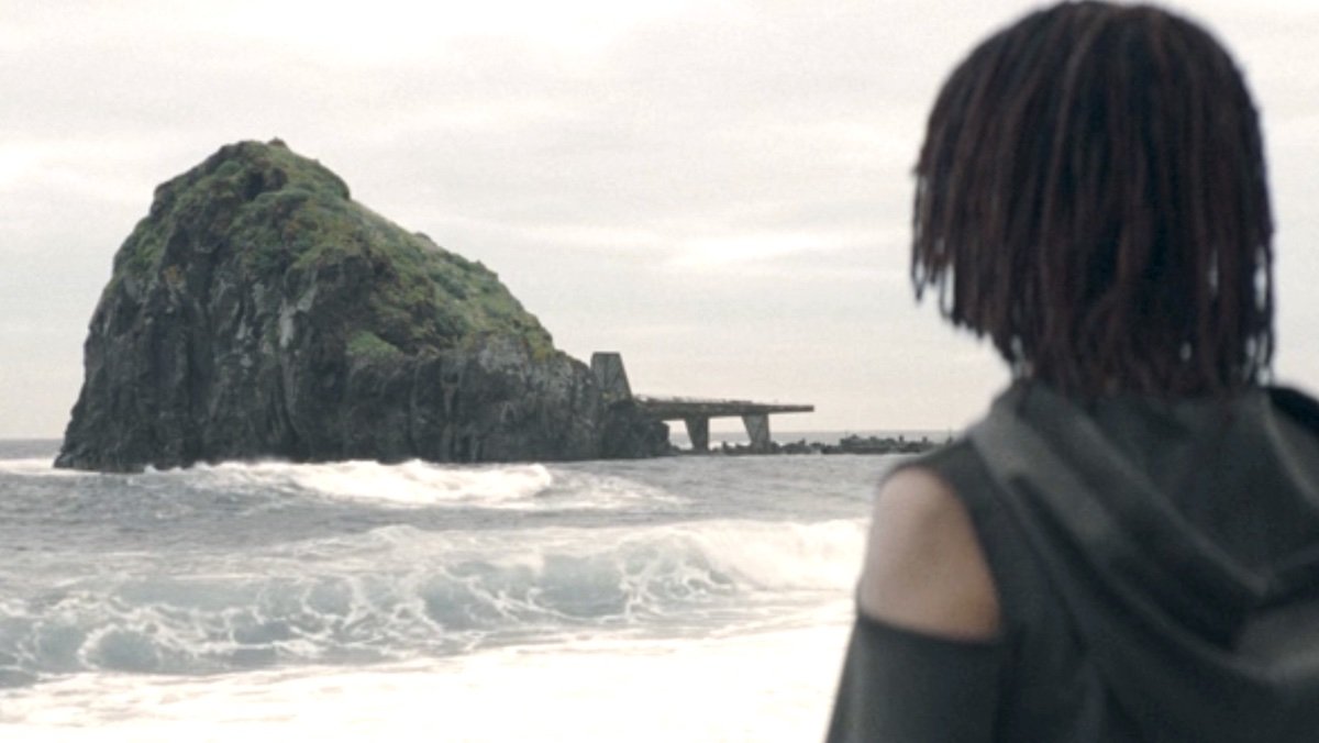 Osha looks out at a ship near a green rocky island on The Acolyte, she is Qimir's unknown planet that may be Ahch-to