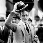 D.W. Griffith, facing the camera, lifts his hat from his head