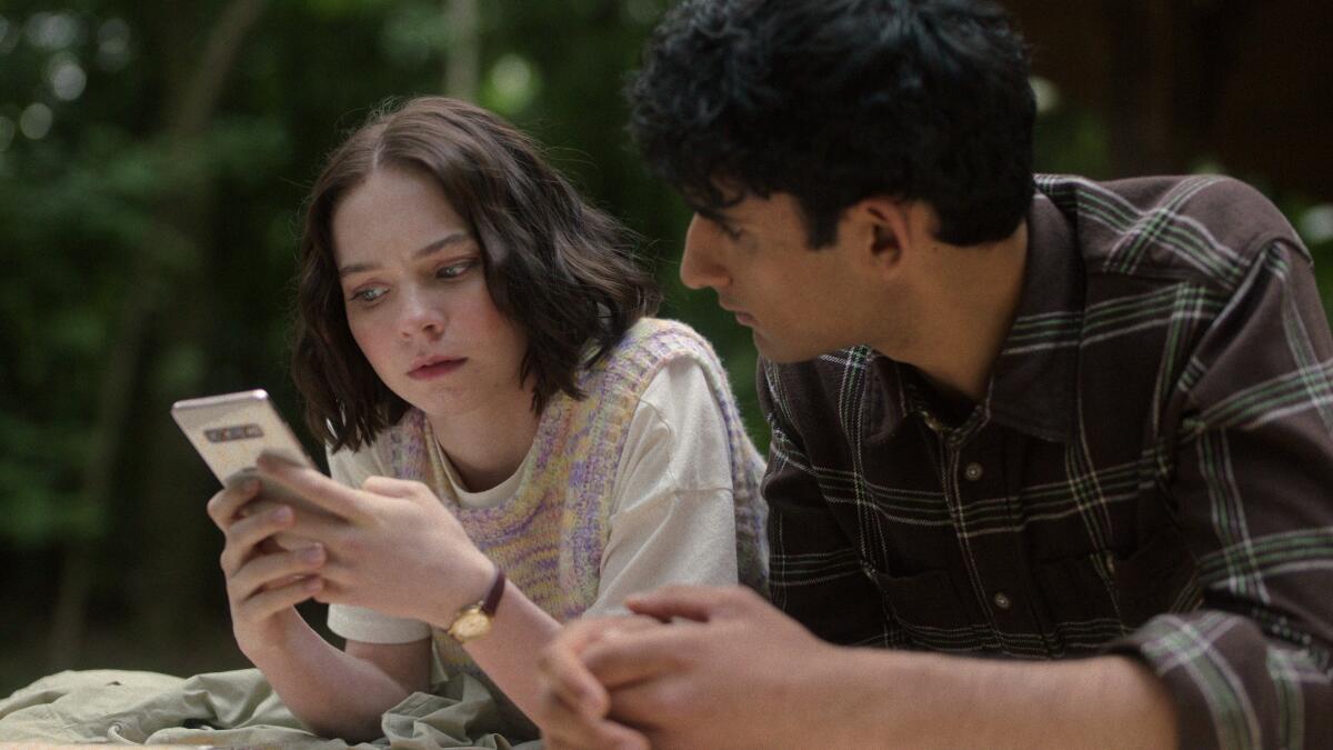 A girl holds a cellphone as a boy looks on beside her