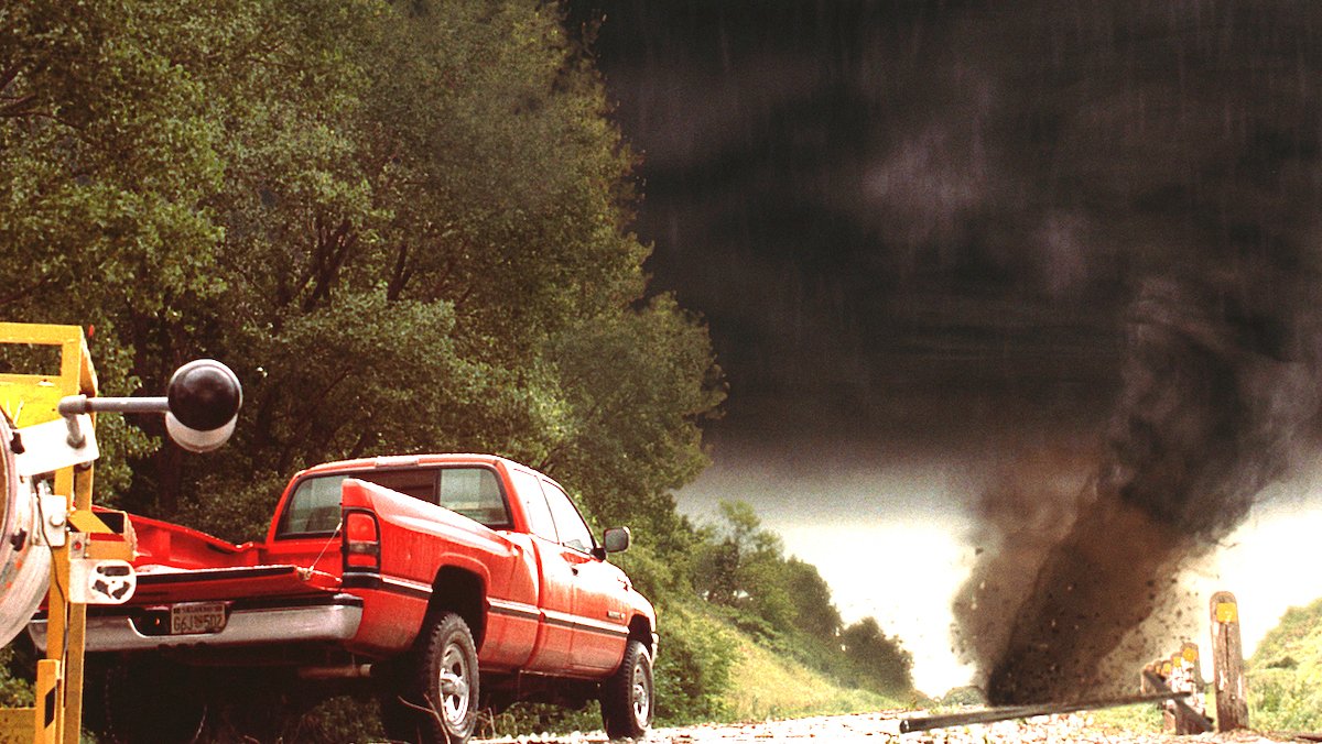 A red pickup truck parked on a street as a tornado comes near in Twister