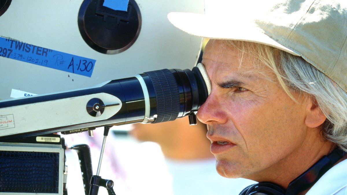 Directro Jan de Bont in a white hat looks through a camera lens while filming Twister