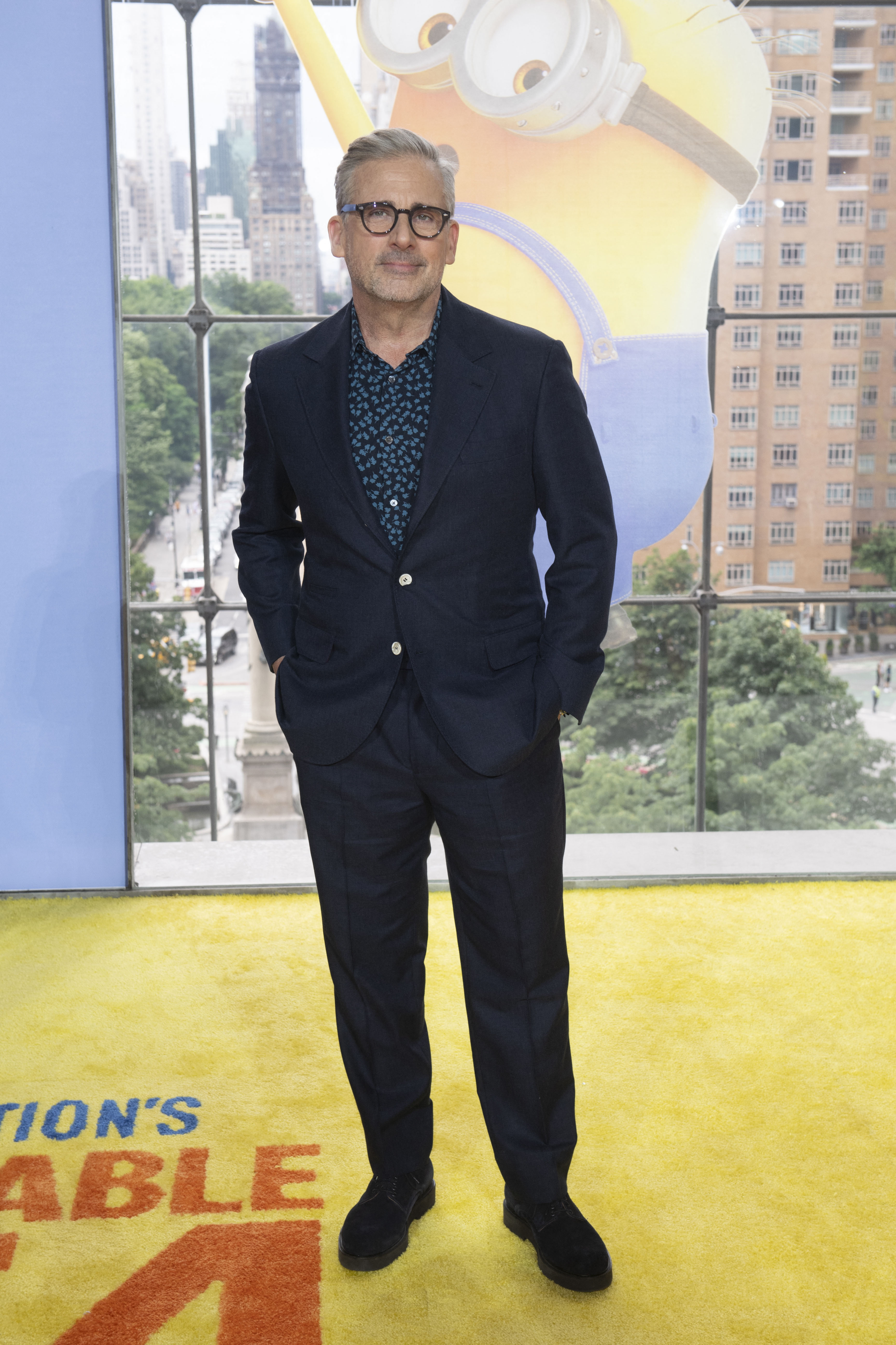 Steve Carell, seen in a sharp black suit with a blue undershirt at the Despicable Me 4 premiere in June 2024, has voiced Gru since the franchise started