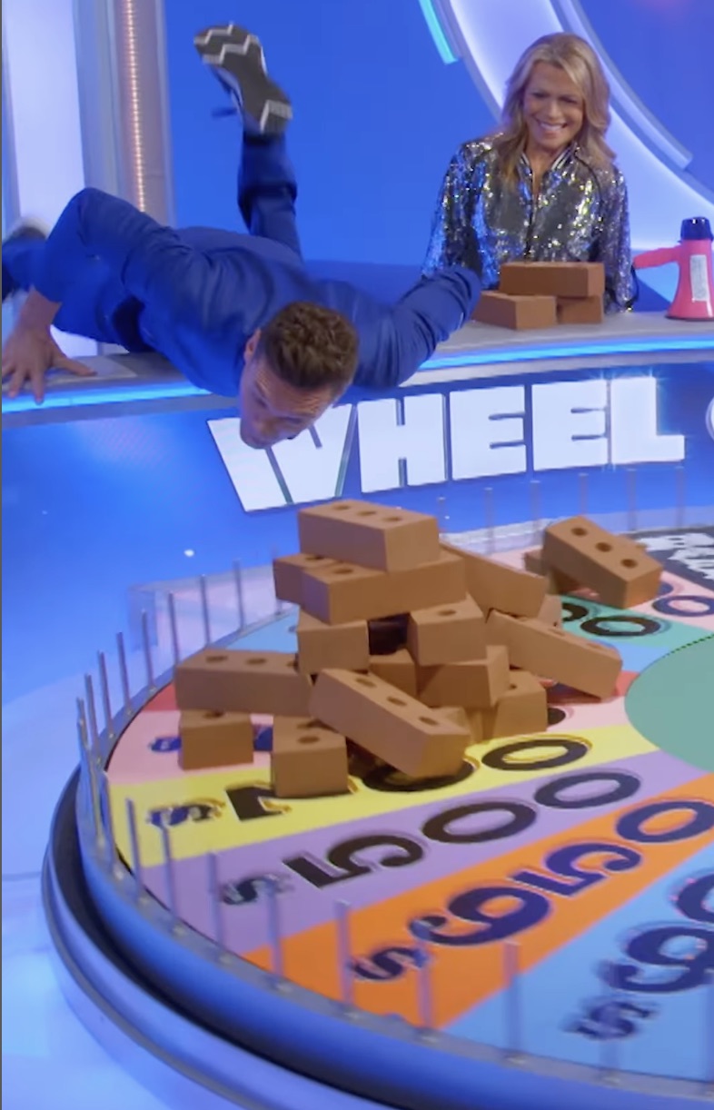 Ryan Seacrest spun the Wheel of Fortune wheel with a pile of bricks on it as Vanna White looked on in a shimmery bomber jacket