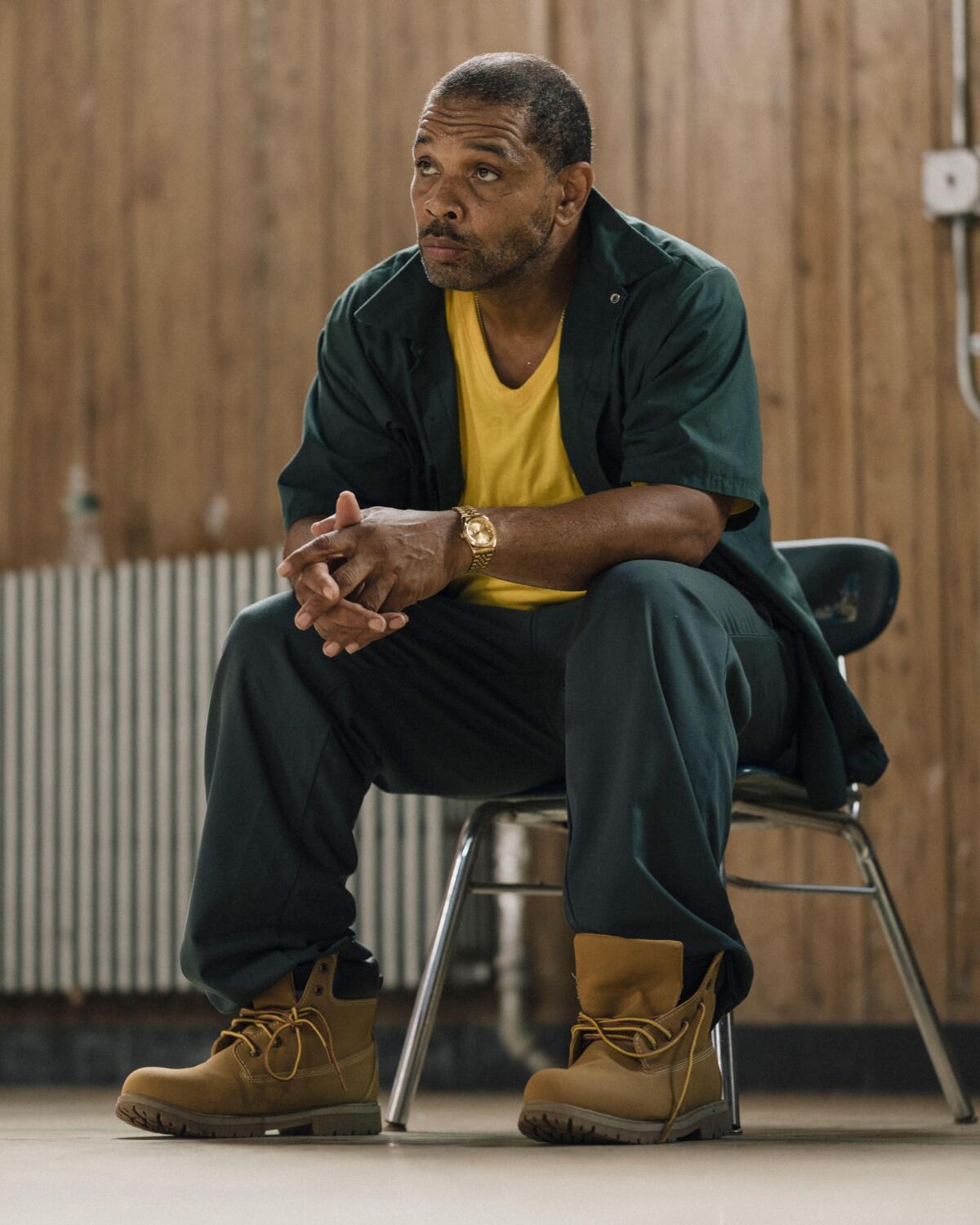 A man in boots and a yellow T-shirt sits in a chair.