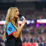 Ingrid Andress sings the national anthem prior to the 2024 Home Run Derby at Globe Life Field in Arlington, Texas, on Monday. She's standing while holding a microphone. In the blurry background is the baseball stadium filled with spectators.