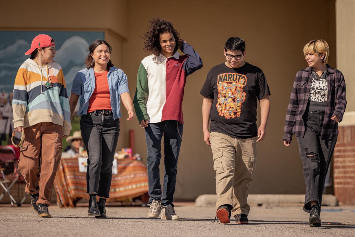 A group of teenagers walk toward the camera five across.