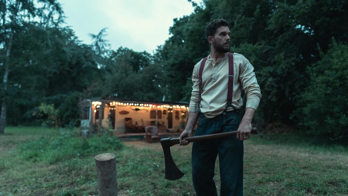 Kit Harington chops firewood while something lurks in the forest in The Beast Within.