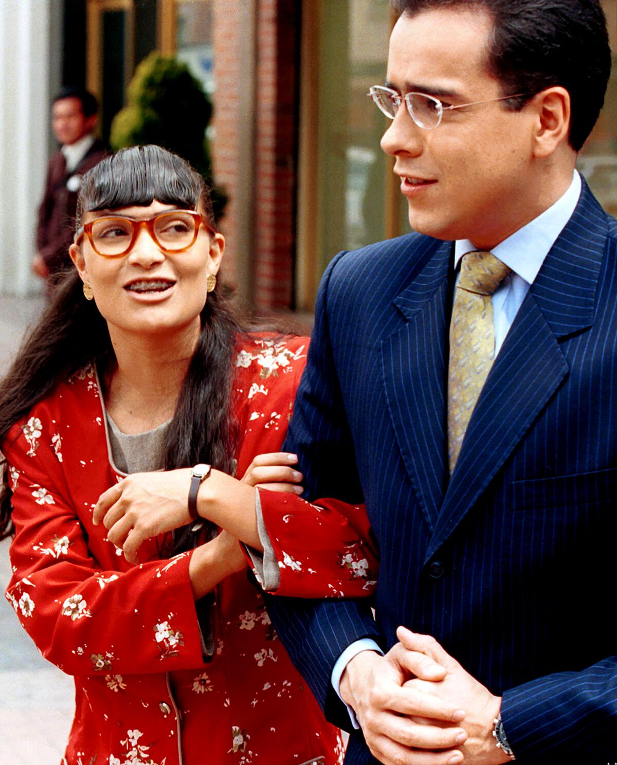 A woman in a red dress and red-rimmed glasses looks the man a suit next to her.