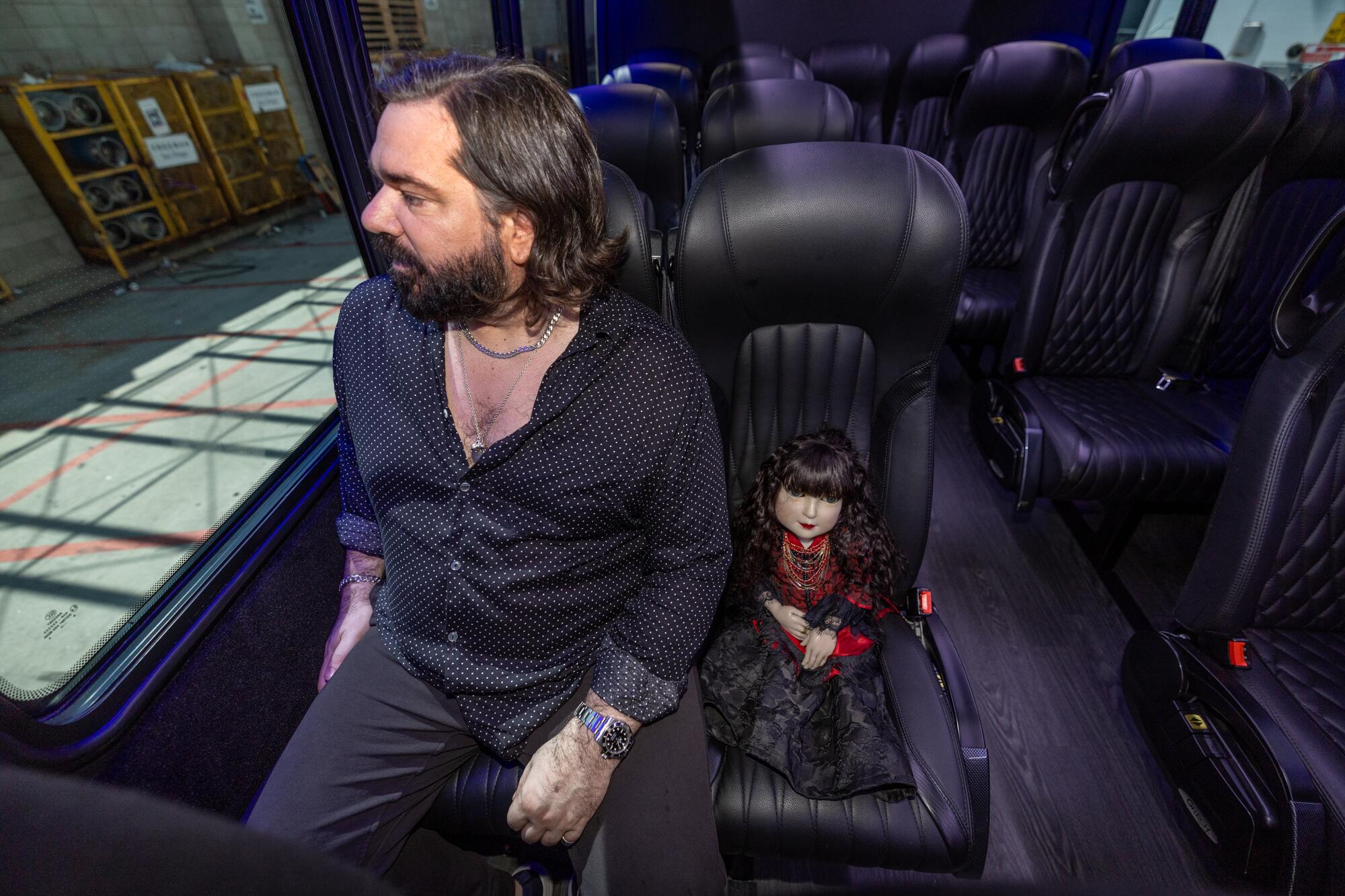 A man shares a bus seat with a small doll prop