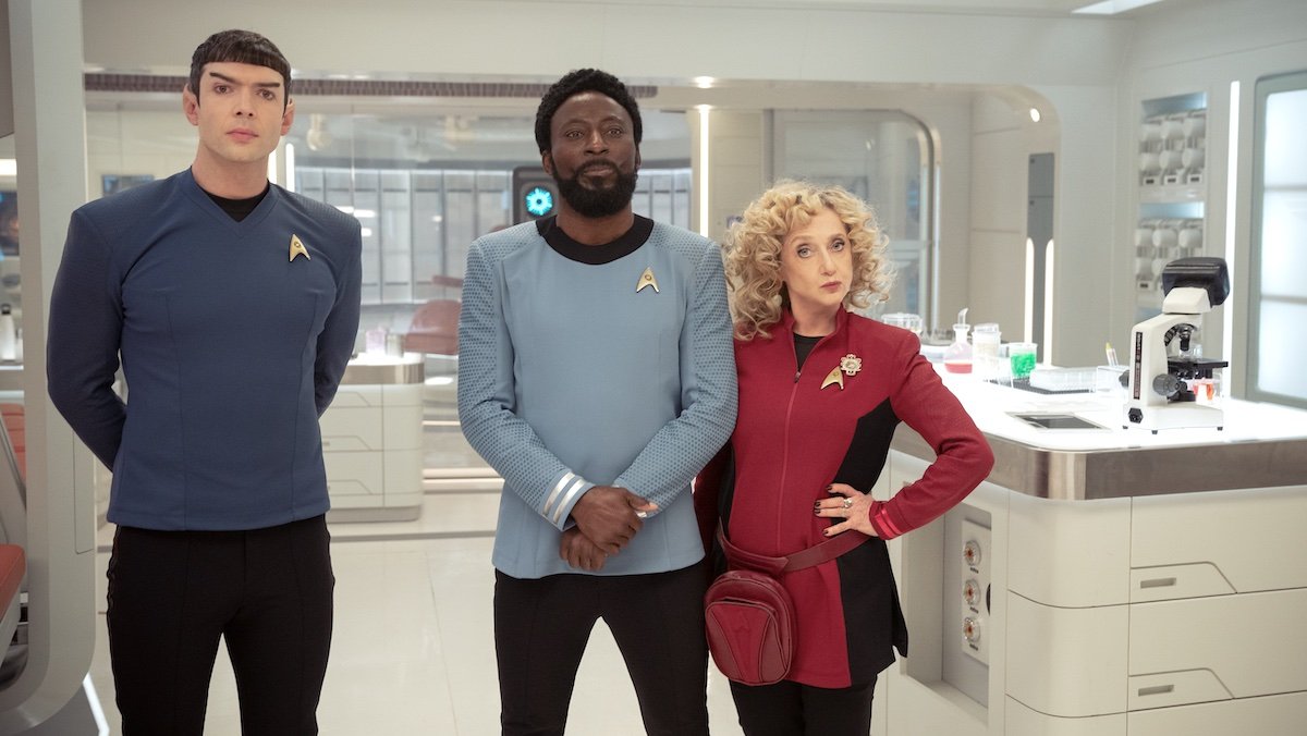 Three characters in Starfleet uniforms standing together in a brightly lit hospital bay on Star Trek: Strange New Worlds
