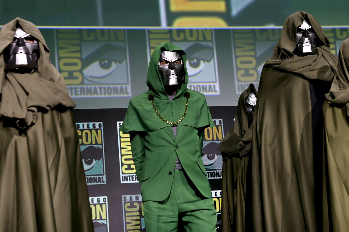 Robert Downey Jr. in a green, hooded suit with a gold chain (very Doctor Doom) wearing a Doctor Doom Mask on stage at the Marvel Studios Panel at SDCC 2024. 