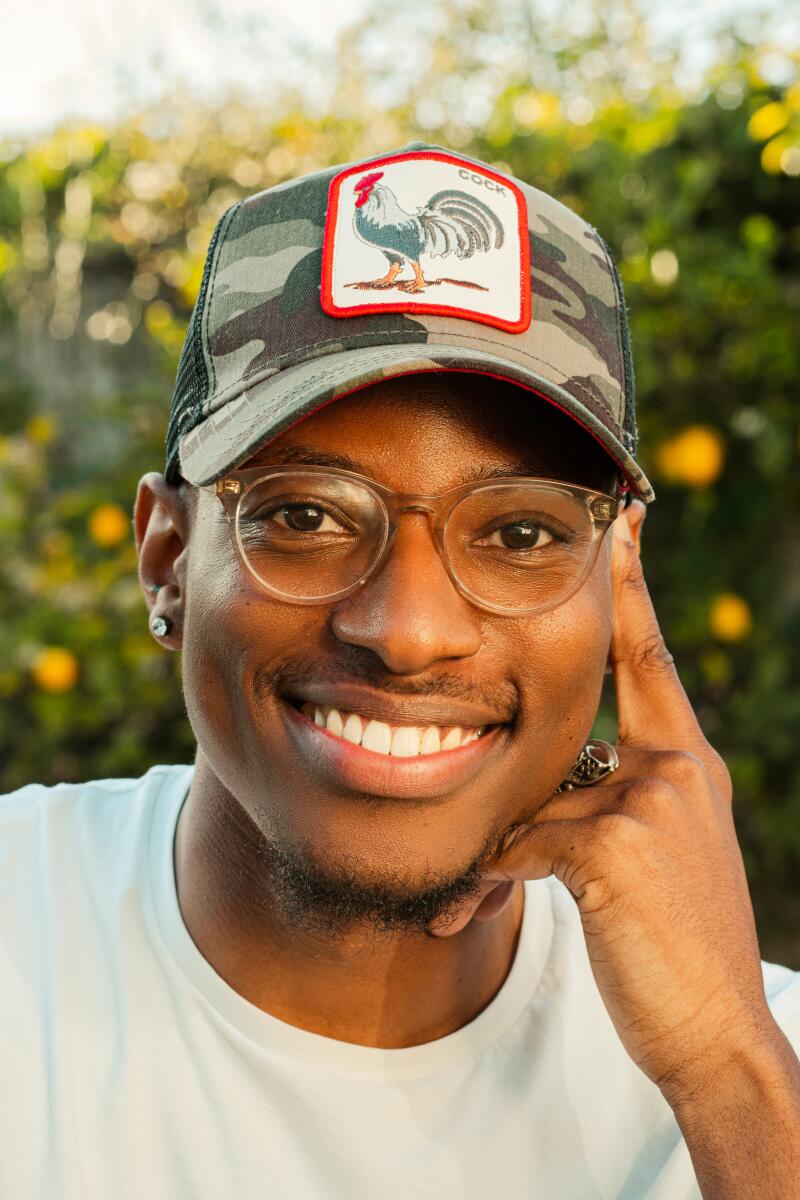 A man in glasses, a cap and a white shirt smiles for the camera.