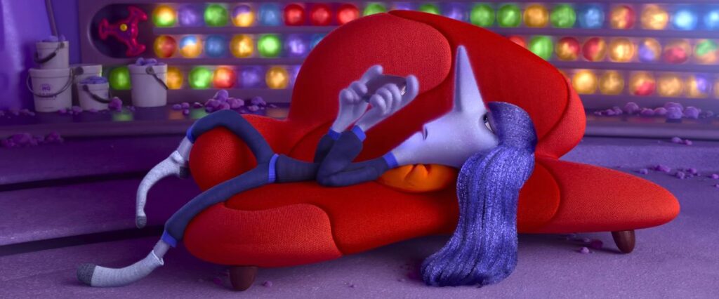 Ennui lounges on her back on a bright red couch, looking irritated and playing with her phone, in a scene from Pixar Animation Studios’ Inside Out 2