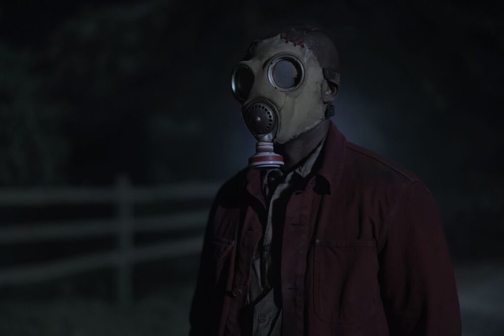 A person with a gas mask standing in a dark road in Peacock’s Teacup