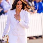 Meghan Markle smiling with her left hand on her chest