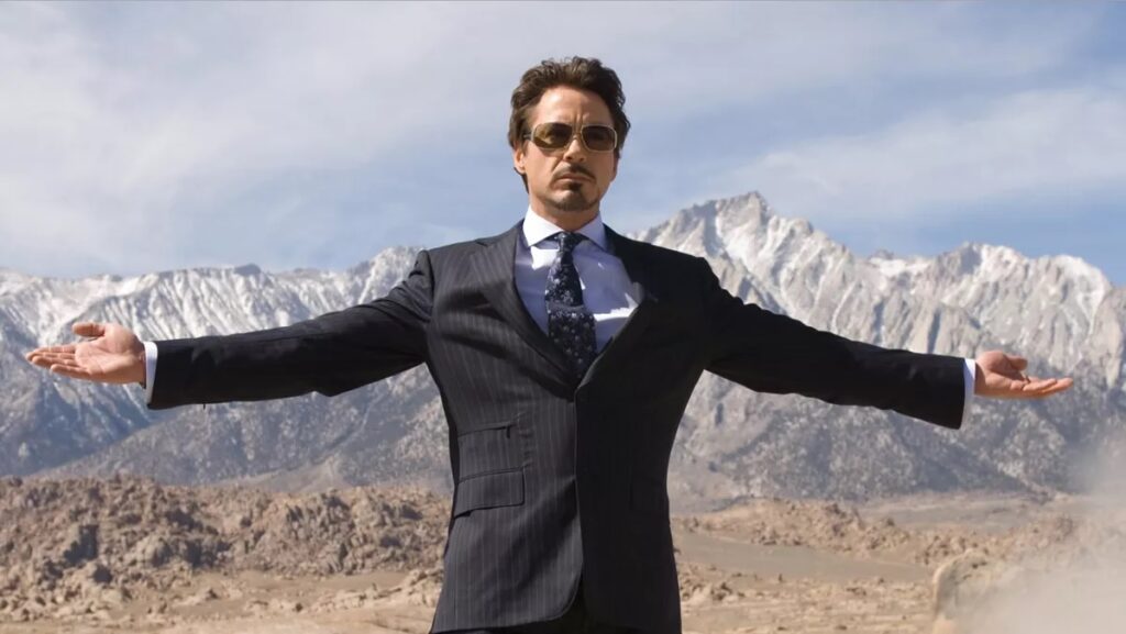 Tony Stark in glasses and a suit with his arms held out wide in Iron Man