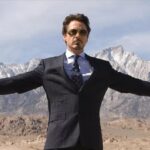 Tony Stark in glasses and a suit with his arms held out wide in Iron Man