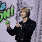 Taemin onstage holds a microphone and gives a thumbs-up.