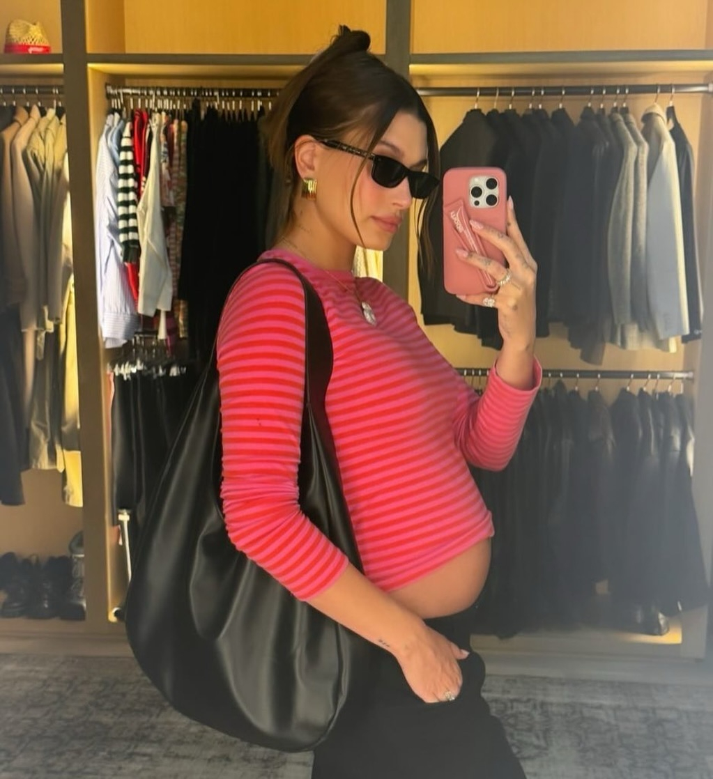 Hailey Bieber snaps a photo showcasing her baby bump in a pink and red striped top
