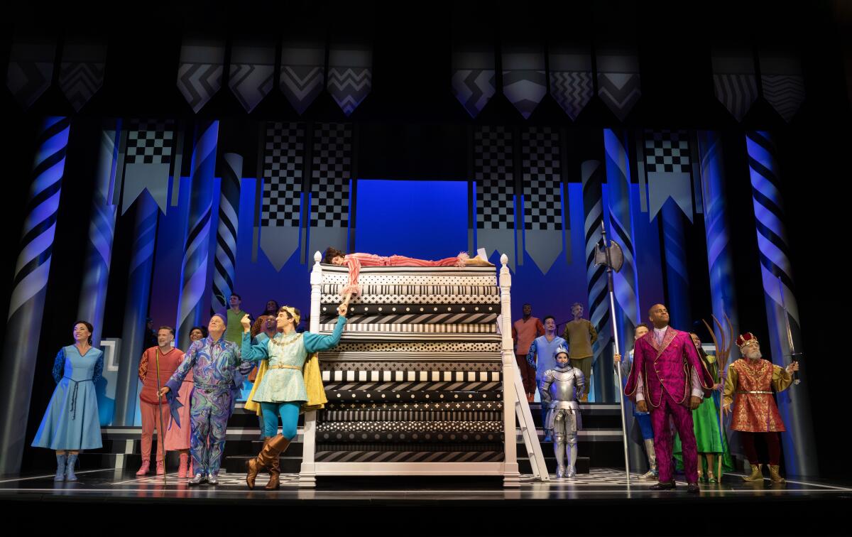 A prince reaches up to a princess lying on a very tall bed with many mattresses, in a stage musical