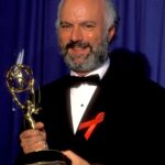James Burrows, with a salt-and-pepper beard and wearing a tux, holds an Emmy statuette with both hands.