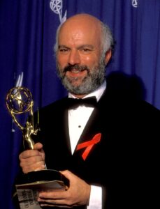James Burrows, with a salt-and-pepper beard and wearing a tux, holds an Emmy statuette with both hands.